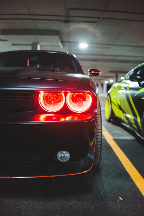 Front of powerful black sports car with switched headlights parked on asphalt ground in indoor parking