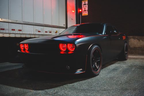 Free Black automobile with red headlight and body kit parked near white van and brick wall in street in evening time Stock Photo