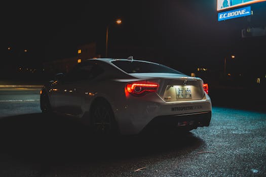 A modern white car with glowing taillights parked on a city street at night.