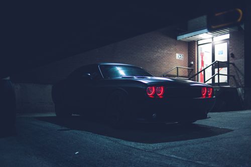Free Low angle of black automobile with red headlights parked on asphalt road near building with brick wall on street at night Stock Photo