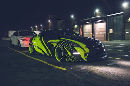 Contemporary black automobile with yellow wrapping decal design and headlights on parking lot in city street at night time outside