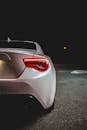 Rear view of modern white automobile with tail light parked on asphalt road on parking lot in dark night in city street