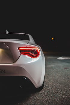 Rear view of modern white automobile with tail light parked on asphalt road on parking lot in dark night in city street