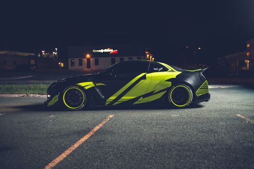 Free Side view of modern black automobile with wrapping decal design on parking lot with marking lines on asphalt in street at night Stock Photo