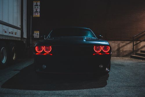 Free Black automobile with red headlights parked on asphalt road near brick wall and van on street at night time outside Stock Photo