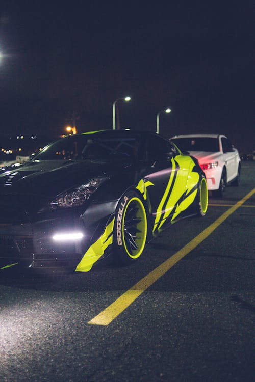 Black modern car with wrapping decal design and headlight light parked on asphalt road with marking line in street at night time