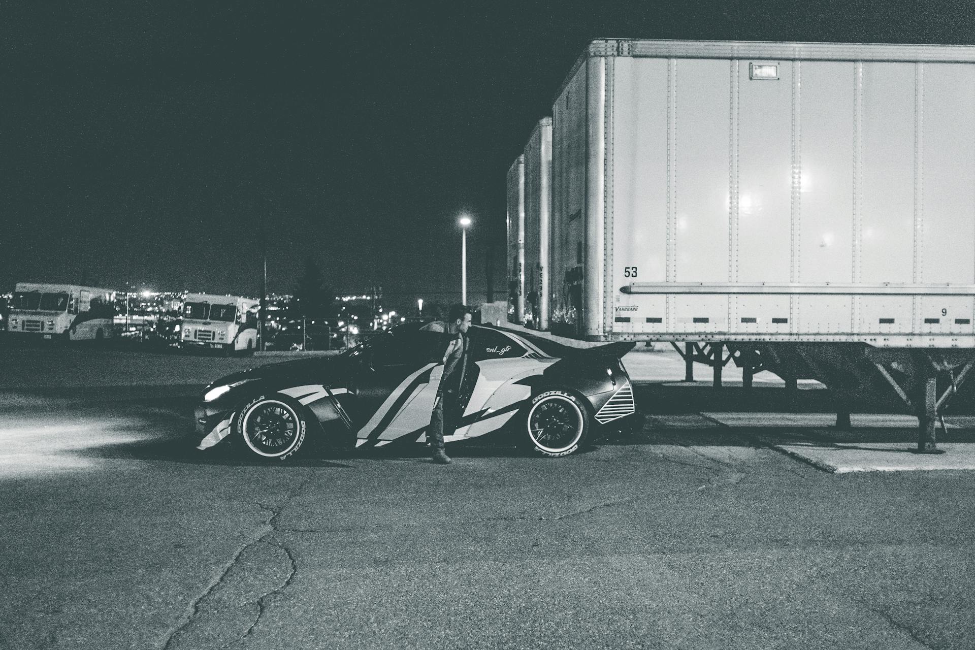 A sleek, modern car parked beside trailers at night in an urban setting.