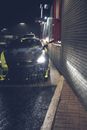 一辆带有黄色条纹和前灯的当代黑色汽车，在雨夜停靠在柏油路上，旁边是一栋有砖墙的建筑
