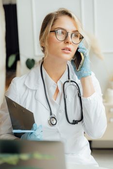 一位穿着白外套、戴着手套的女医生正在医疗办公室里打电话