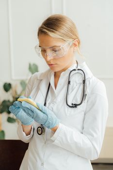 医疗机构内，一名女医生戴着听诊器和防护眼镜，正在使用智能手机
