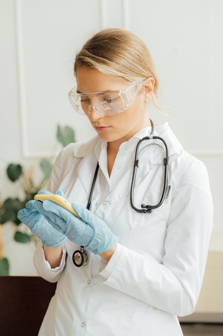 Doctor Looking At Her Phone While Wearing Latex Gloves