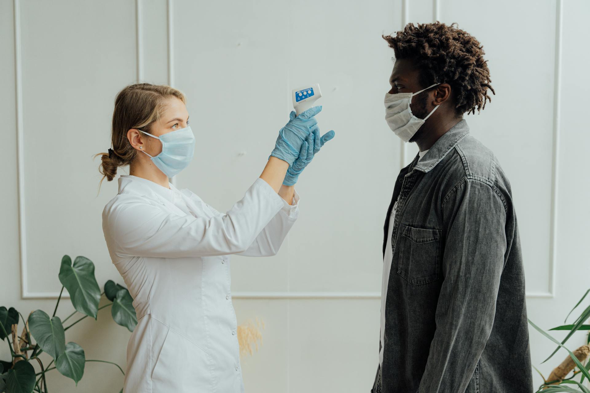 A healthcare worker measures a patient's temperature with a forehead thermometer.