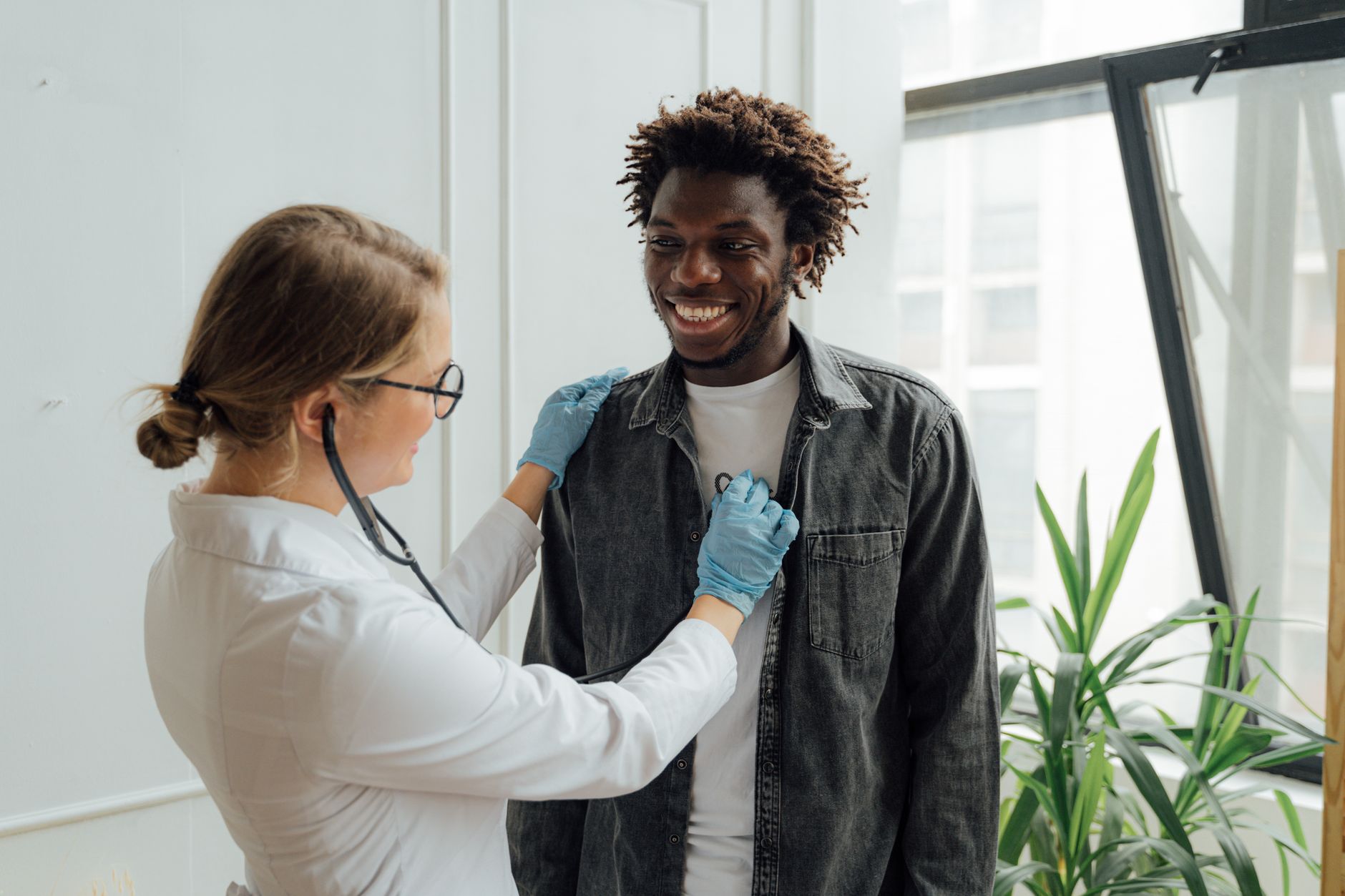 Doctor with stethoscope examining a smiling patient indoors, promoting health and care.