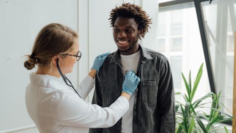 Doctor with stethoscope examining a smiling patient indoors, promoting health and care.