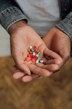 A close-up image of hands holding various colorful capsules and tablets, symbolizing medication or supplements.
