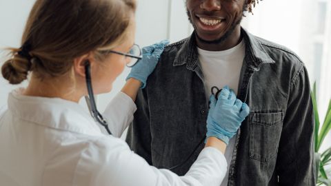 A doctor uses a stethoscope on a smiling patient in a bright room, indicating a positive medical experience.