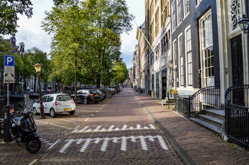 Free Empty paved bicycle road and sidewalk between aged residential buildings and canal in sunny morning in Amsterdam Stock Photo