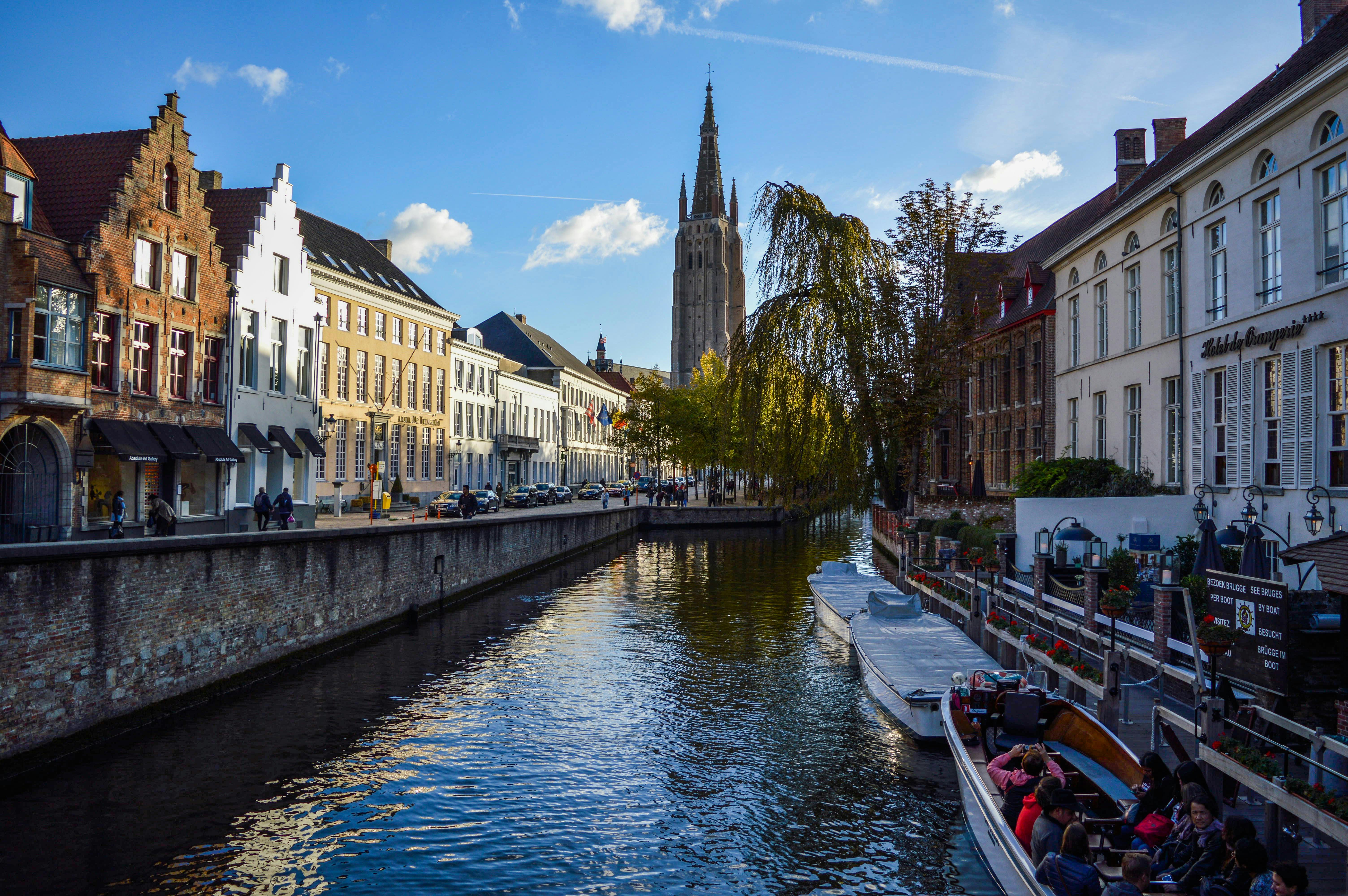 Picturesque scenery of rippling canal flowing near aged typical houses and historical Church of Our Lady against blue sky in Bruges