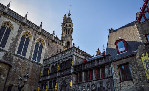 From below exterior of medieval Basilica of the Holy Blood with amazing ornamental design and tower against cloudless blue sky in Bruges