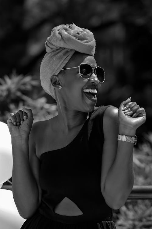 Black and white glad young African American female with mouth opened wearing trendy sunglasses turban and dress smiling happily