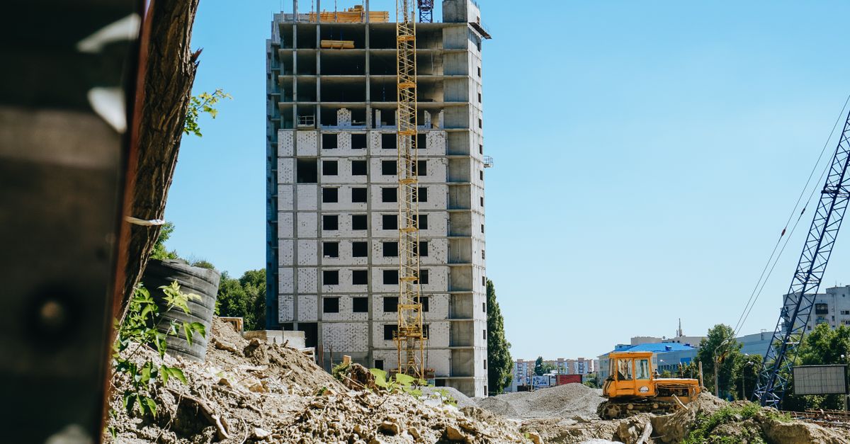 Mid-rise building under construction with cranes and machinery in a cityscape.