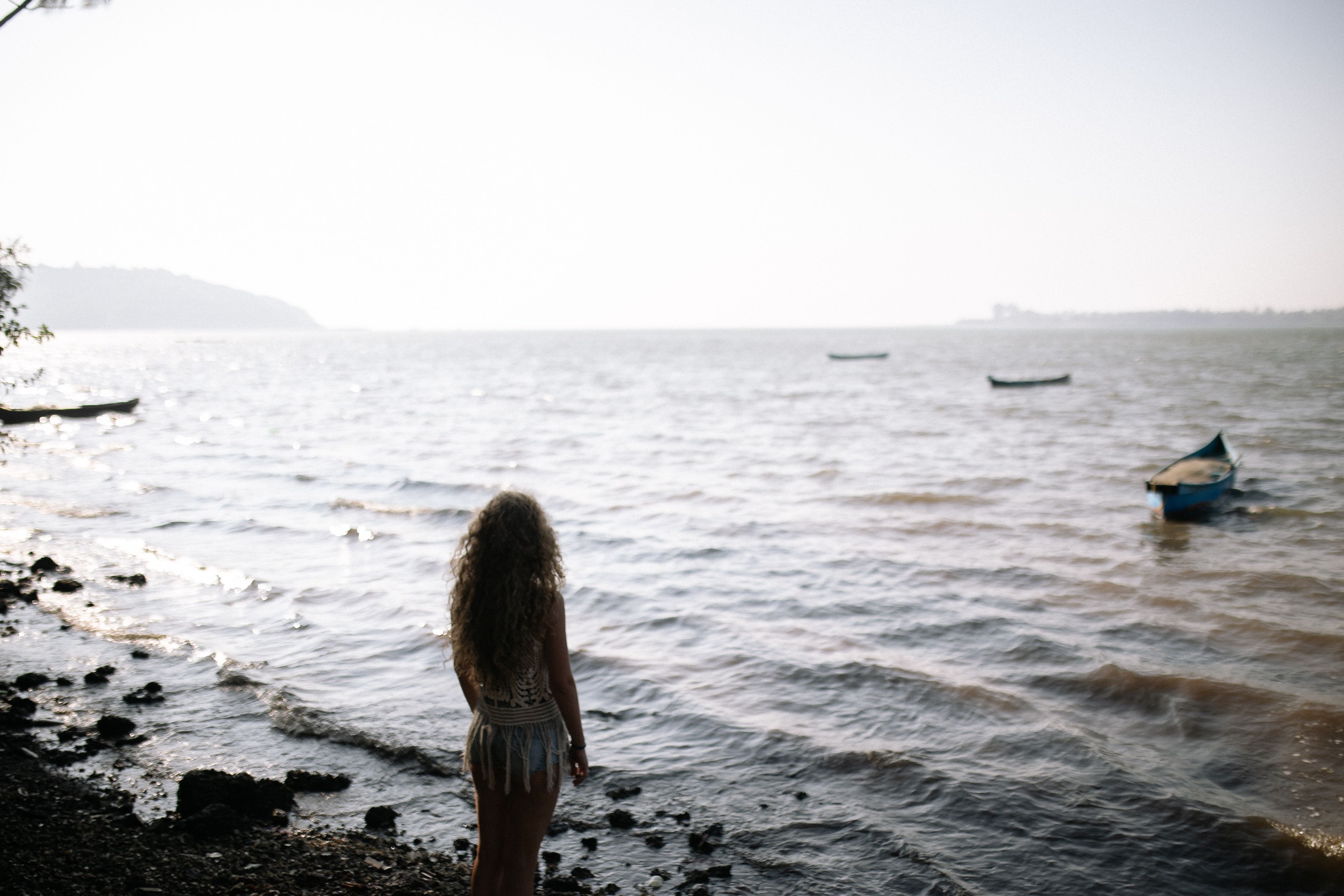 在宁静的海滩上，一名女子凝视着漂浮在海面上的船只