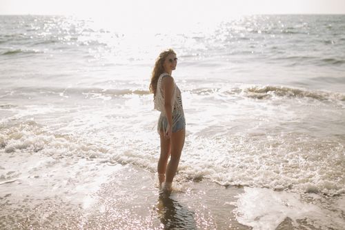 Free Woman standing in ocean waves wearing sunglasses, exuding a relaxed summer vibe. Stock Photo