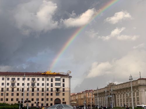 Free A vibrant rainbow arches over historic city buildings against a dramatic sky. Stock Photo