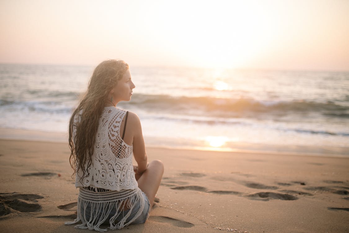 Free Woman in a Lace Blouse Sitting on a Sandy Beach Stock Photo