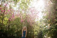 Woman in Blue Long Sleeve Shirt and Blue Denim Jeans Standing Under Pink Cherry Blossom Tree