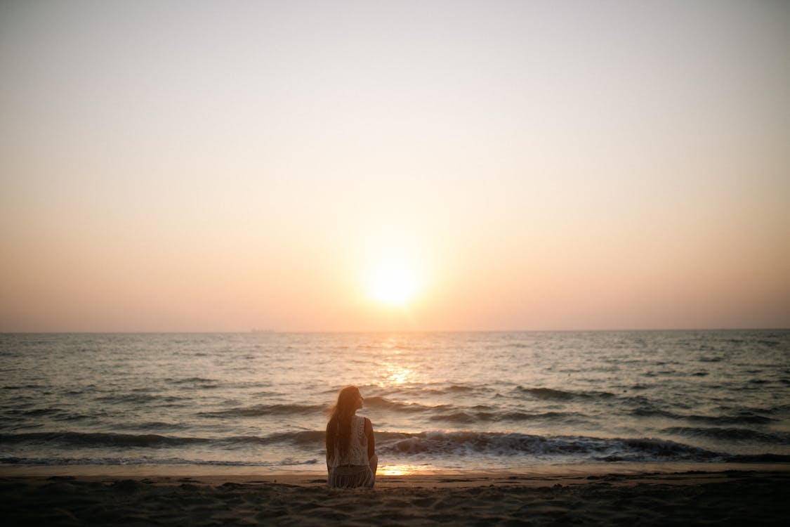 Free Woman Sitting on the Beach during Sunset Stock Photo
