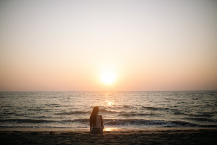 Woman Sitting On The Beach During Sunset