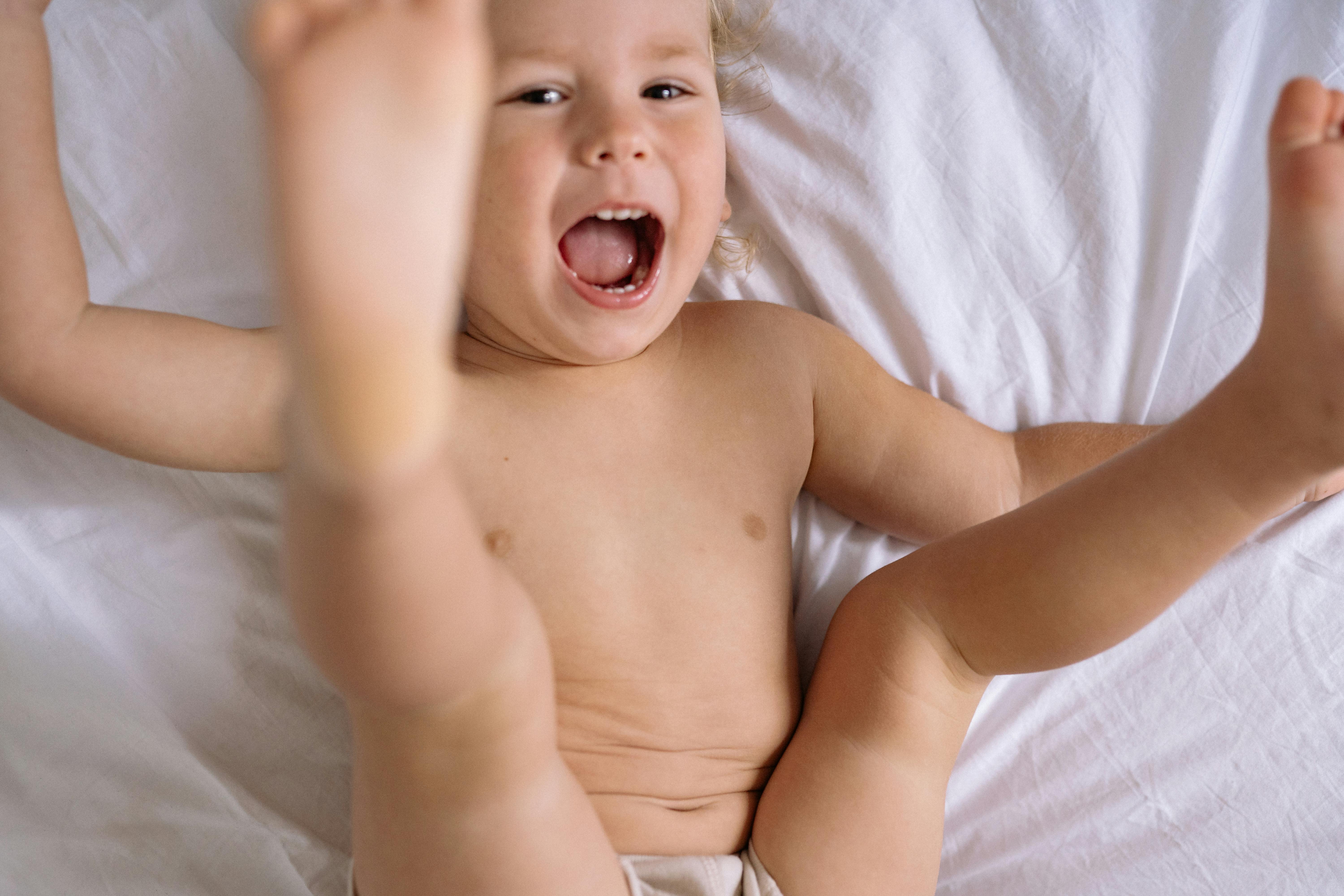 topless toddler lying on white bed