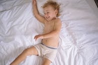 Baby in White and Blue Shorts Lying on White Bed