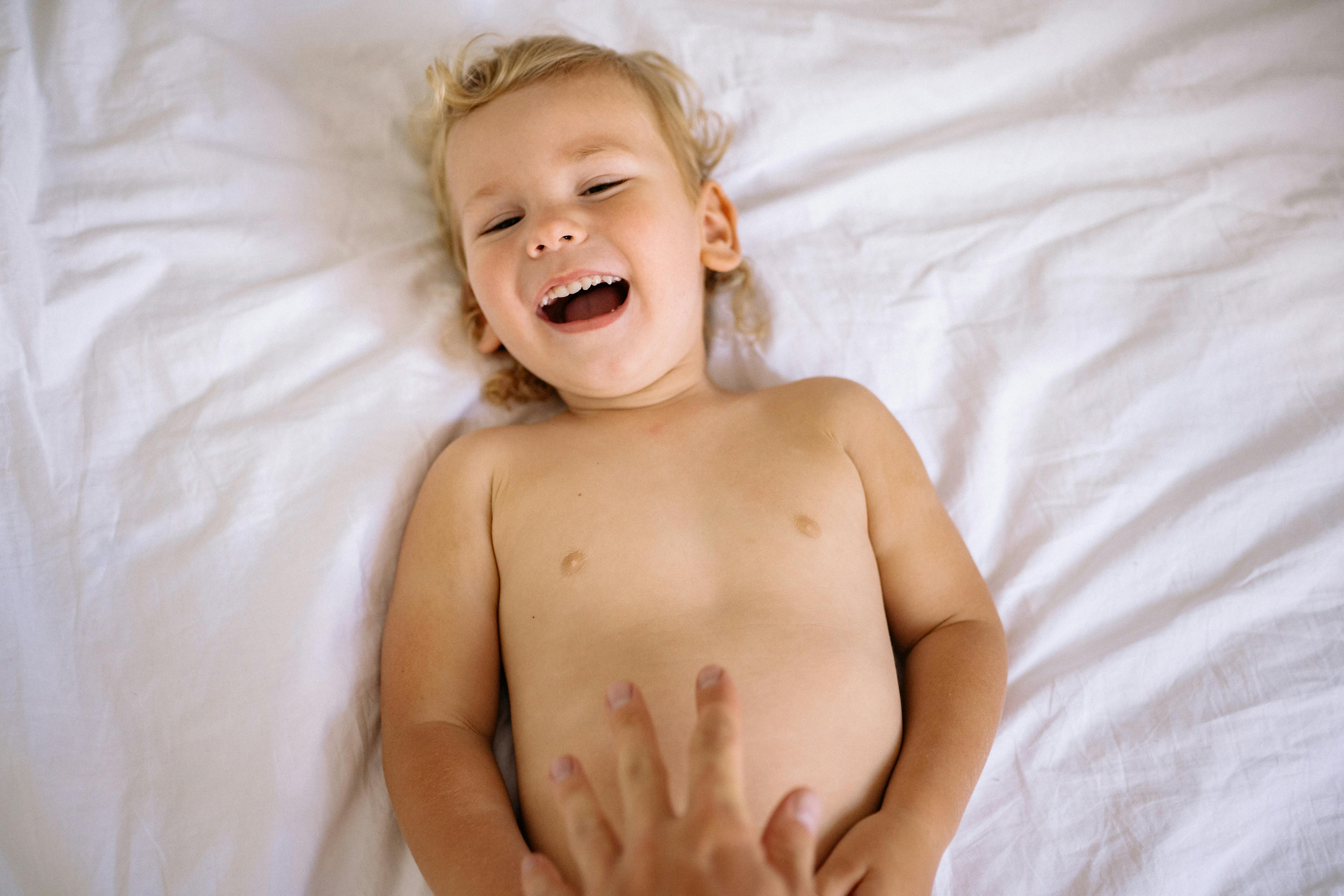 topless baby lying on white textile