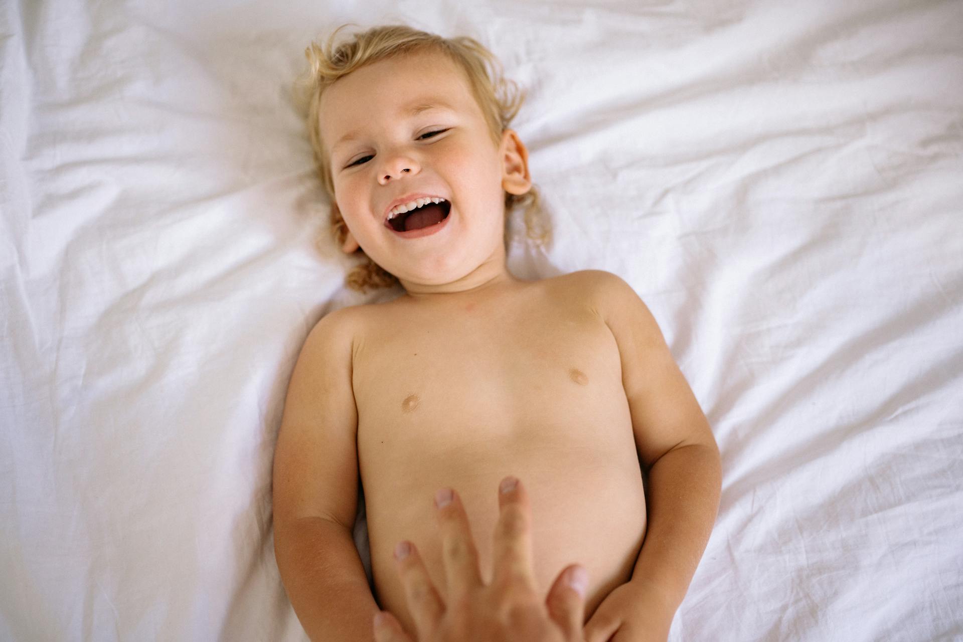 A joyful child laughing while lying on a clean white bed indoors, creating a warm and playful atmosphere.