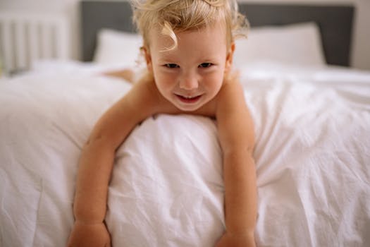 Smiling toddler lying on a bed with white sheets, exuding happiness and innocence.
