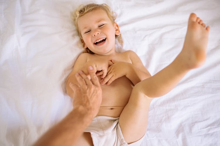 Blonde Boy Lying On A Bed And Giggling