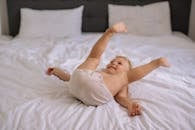 Baby in White Tank Top Lying on White Bed