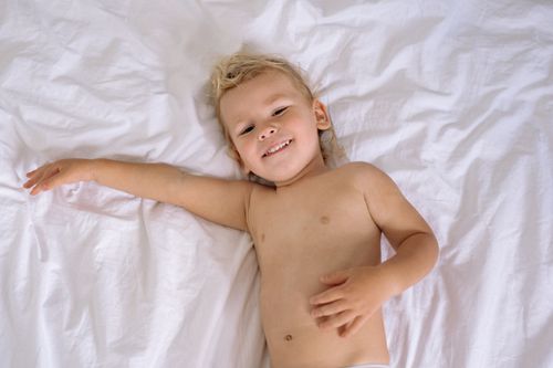 Free A joyful young child lying on white sheets, smiling while relaxing comfortably indoors. Stock Photo