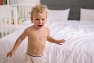 一个快乐的幼儿在明亮的卧室里开心玩耍，捕捉到了儿时顽皮的快乐瞬间