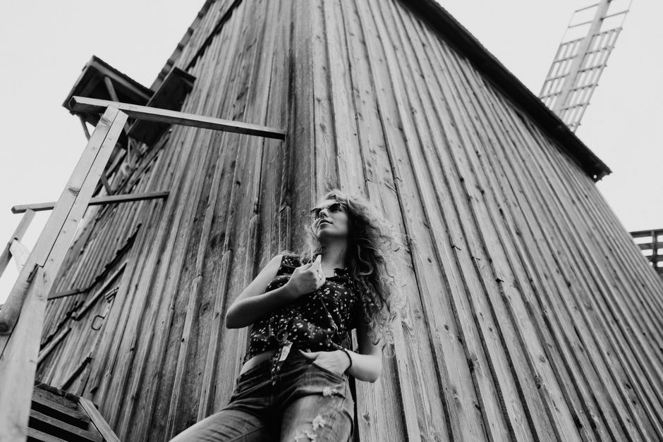 Young woman poses confidently in front of a rustic wooden structure, exuding style and modern fashion.