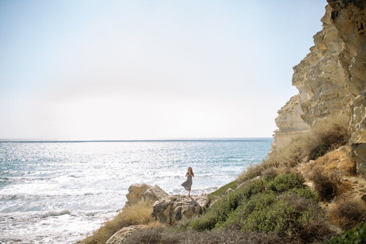 A Woman Standing One Leg On A Rock Near Coast