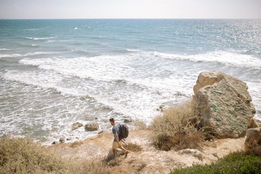 A man walks along a coastal path with ocean waves and rocky landscape in the background.