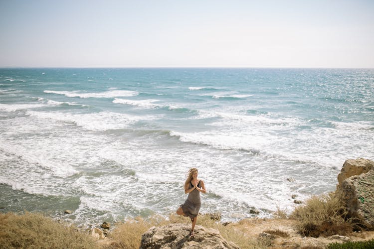 A Woman Standing On A Rock With One Leg Near Sea