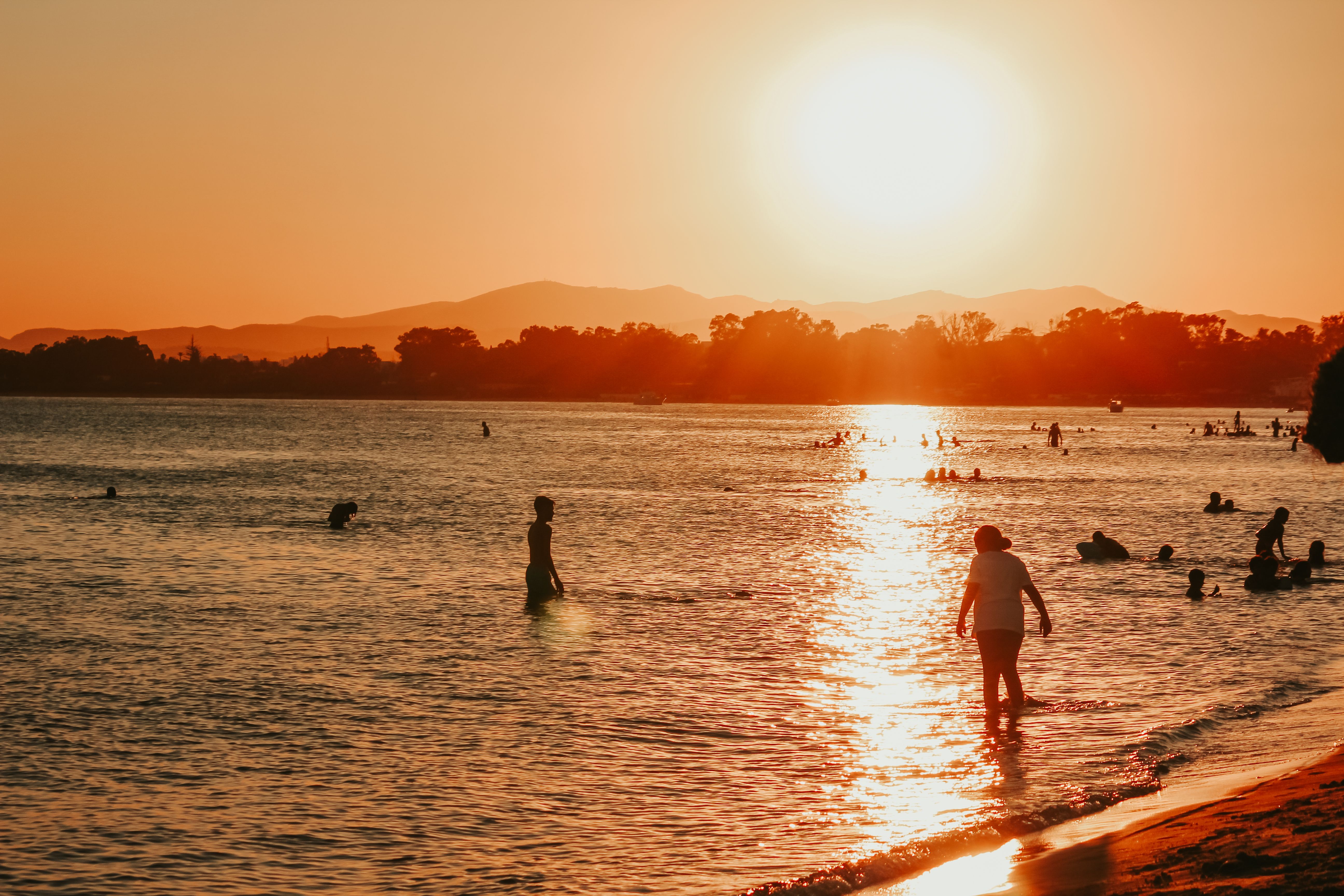 People silhouetted against a vibrant sunset on a peaceful beach shore, capturing the essence of summer.