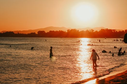 People silhouetted against a vibrant sunset on a peaceful beach shore, capturing the essence of summer.