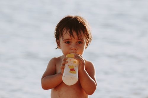 Free A cute child sipping from a bottle at the beach, showcasing innocence and playfulness. Stock Photo