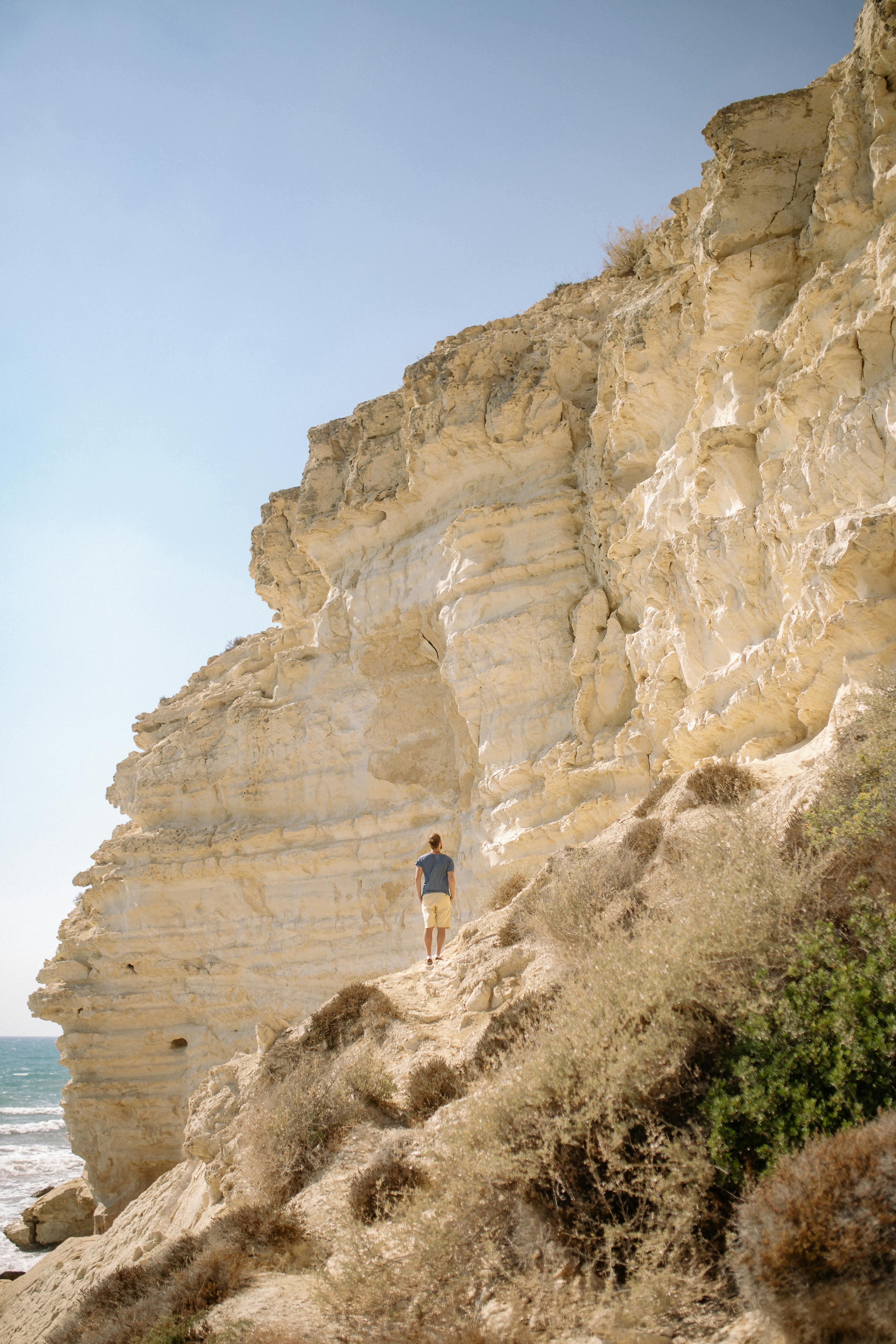 在一个阳光明媚的日子里，一名男子沿着海岸的岩石悬崖徒步旅行