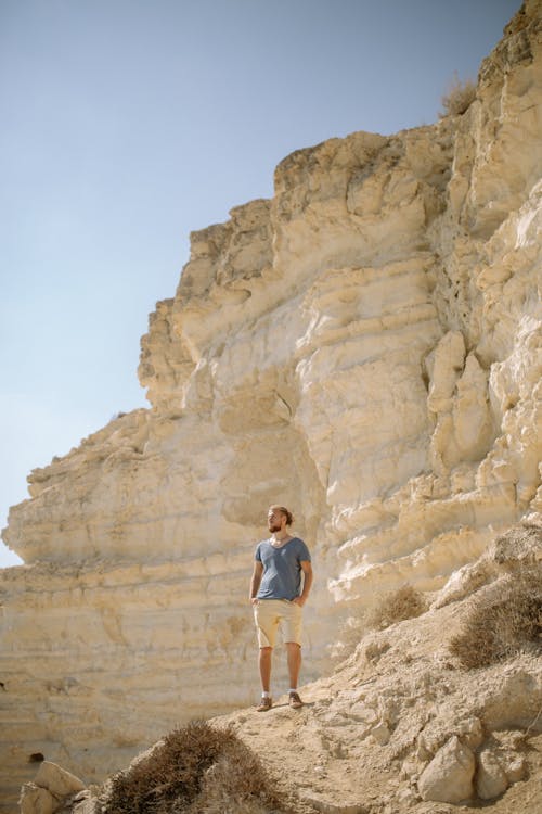 Free Blue Sky above a Man Standing on a Rocky Cliff Stock Photo